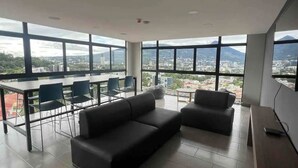 Ein geräumiges Zimmer mit großem Tisch und Stühlen, einer Sitzecke und Blick auf eine Stadtlandschaft durch große Fenster.