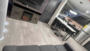 Ein modernes Wohnzimmer mit grauem Sofa, Flachbildfernseher, Kamin und einer Küchenzeile im Hintergrund.
