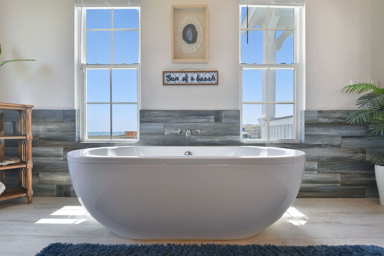 A large freestanding bathtub in a bathroom with a view of the beach through large windows.