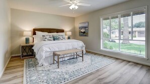Une chambre à coucher avec un lit, des lampes de chevet, un ventilateur de plafond, une fenêtre avec des stores et une vue sur l’extérieur.