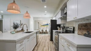 Une cuisine moderne avec des meubles blancs, un îlot central, des luminaires suspendus et une vue sur la salle à manger.