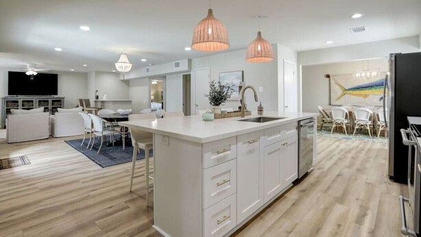 Une cuisine moderne avec des meubles blancs, un îlot central, des luminaires suspendus et un coin repas avec des chaises blanches.