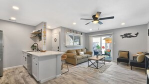 Una cocina moderna con una isla central, un comedor con sofá y sillas, y una sala de estar con ventilador de techo.