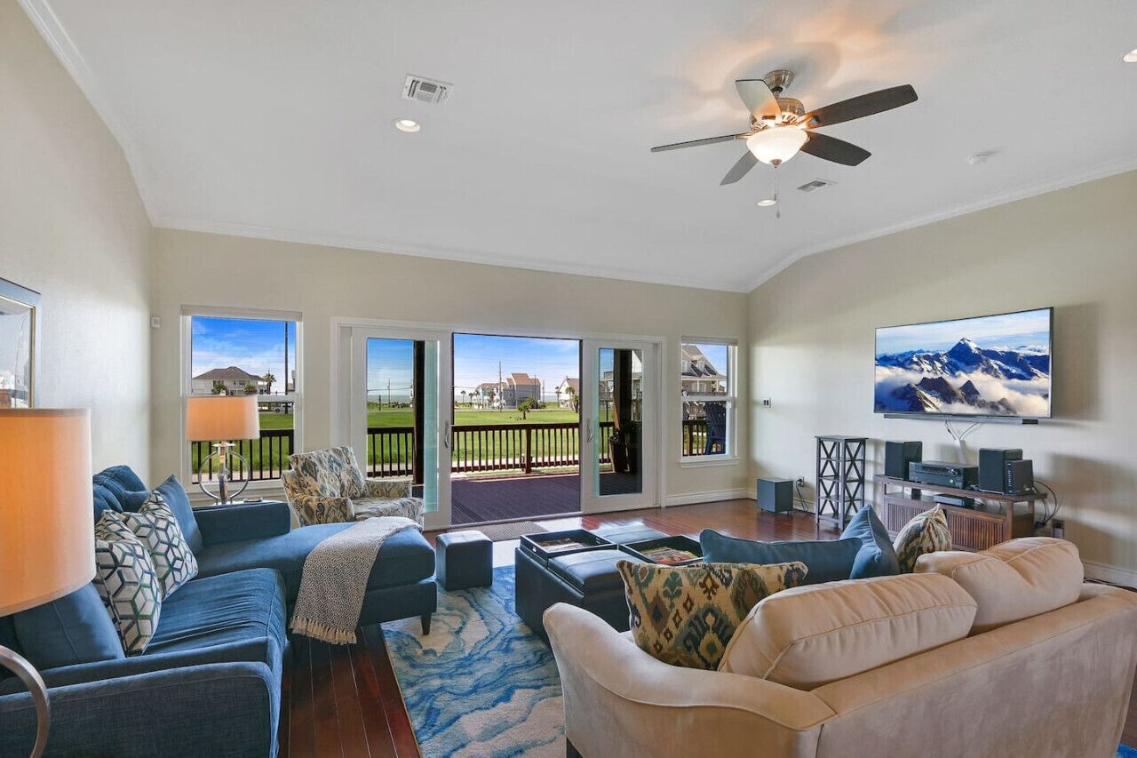 A spacious living room with a large flat-screen TV, comfortable seating, and a balcony with a scenic view.