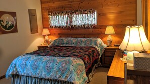 Une chambre à coucher avec une tête de lit en bois, des rideaux à motifs floraux, une couvre-lit à motifs, deux lampes de chevet et une table de chevet avec une lampe.
