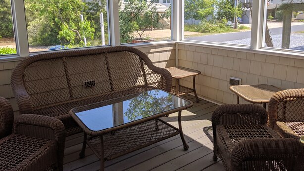 Une véranda aménagée avec des meubles en osier, notamment un canapé et des fauteuils, ainsi qu’une table en verre.