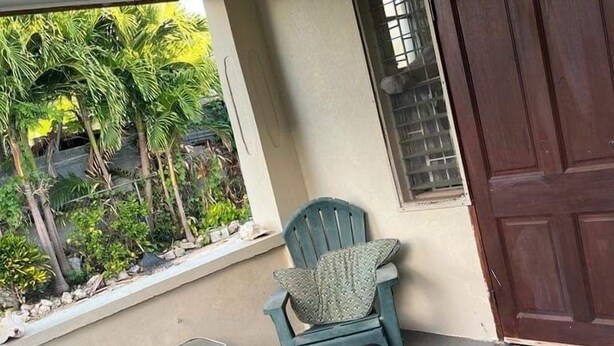 A porch with two green chairs, a small table, and a brown door. - Charming 2-bed Villa in The Garden (Holetown)