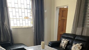 A living room with a black leather sofa, a white coffee table, and a black leather sofa with patterned cushions. - Charming 2-bed Villa in The Garden (Holetown)
