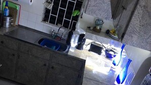 A kitchen with a central island, a sink, and a window with bars. There are various kitchen appliances and items on the countertops. - Charming 2-bed Villa in The Garden (Holetown)
