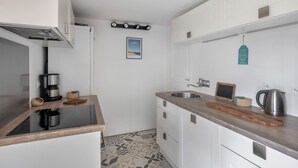Een moderne keuken met een zwart inductiefornuis, een koffiezetapparaat, een waterkoker en een houten snijplank op het aanrecht.