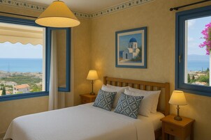 A hotel room with a bed, two bedside lamps, a framed picture of a blue-domed building, and a view of the sea and cityscape through large windows.