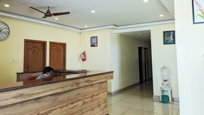 Un área de recepción con mostrador de madera, ventilador de techo, un reloj y extintor en la pared.