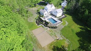 Una casa grande y blanca de dos pisos con piscina, rodeada de exuberante follaje.