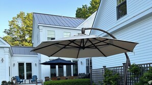 Un patio con mobiliario exterior, una pérgola con toldo y una casa al fondo.