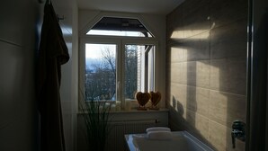A bathroom with a skylight, a bathtub, a radiator, and a window with a view of trees and buildings.