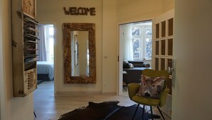 A room with a 'WELCOME' sign, a mirror with a rustic frame, a green chair with a deer pillow, and a bed in the background.