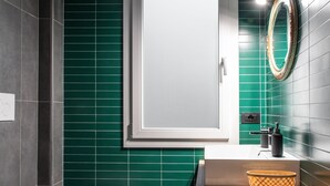 A modern bathroom with a white toilet, a sink with a mirror above it, and green tiled walls.