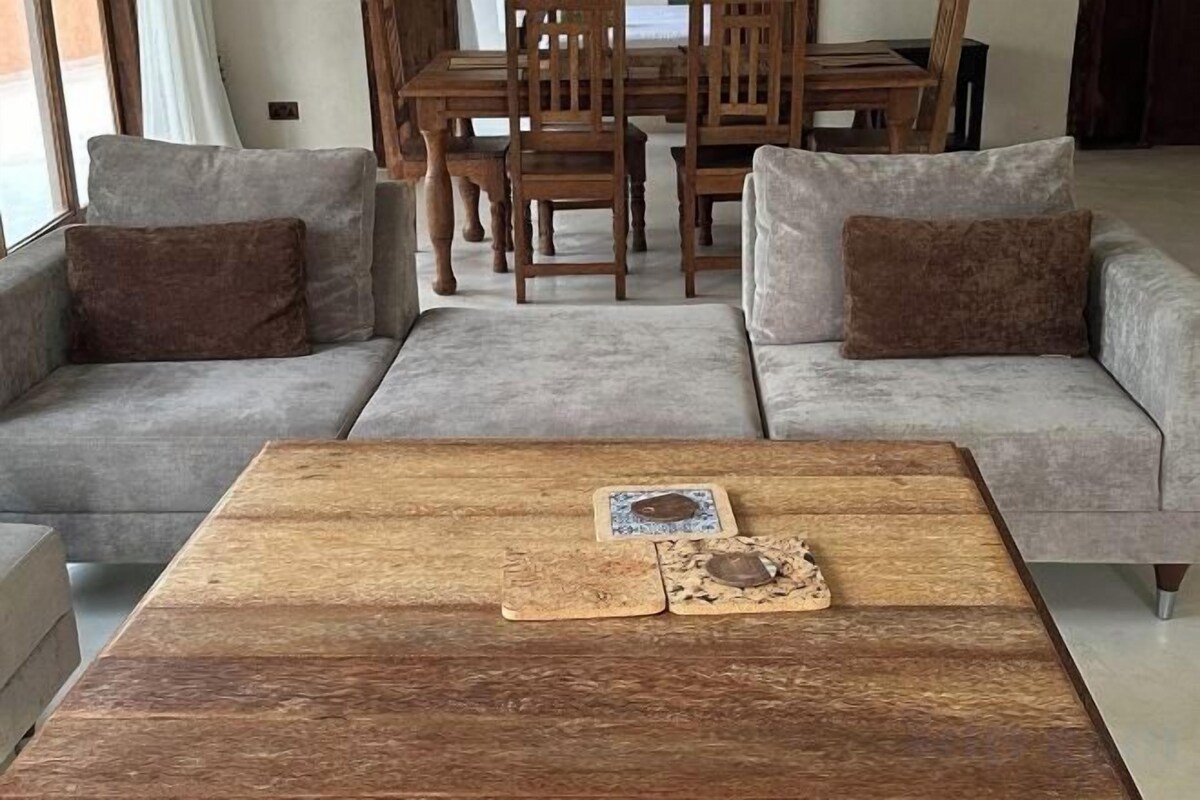 A living room with a grey sofa set, a wooden coffee table, and a dining area with wooden chairs and a table.