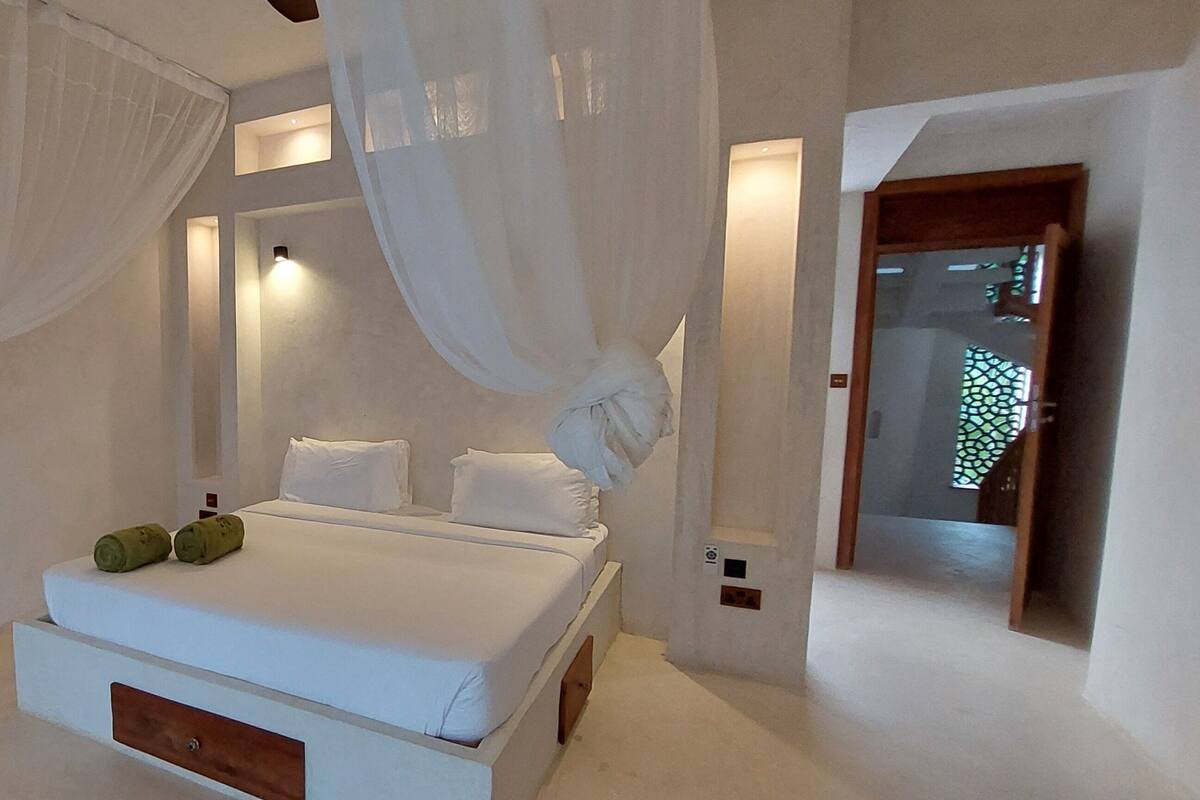 A bedroom with a bed, white curtains, and a wooden chair.