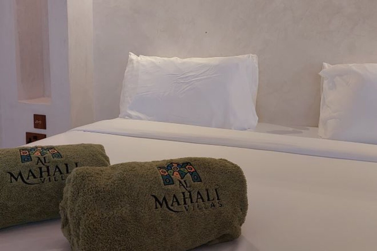 A hotel room with a bed, white pillows, and two towels with the hotel's logo.