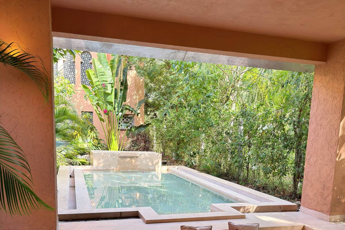 A modern outdoor seating area with a pool, surrounded by lush greenery.