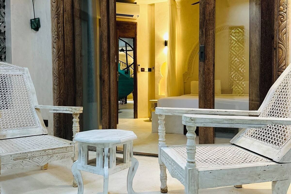 A room with a pool, white wicker furniture, and a large wooden door.