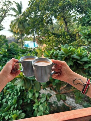 Una persona sosteniendo dos tazas con un jardín tropical de fondo.