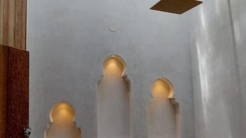 A bathroom with a skylight, a showerhead, and three illuminated niches.