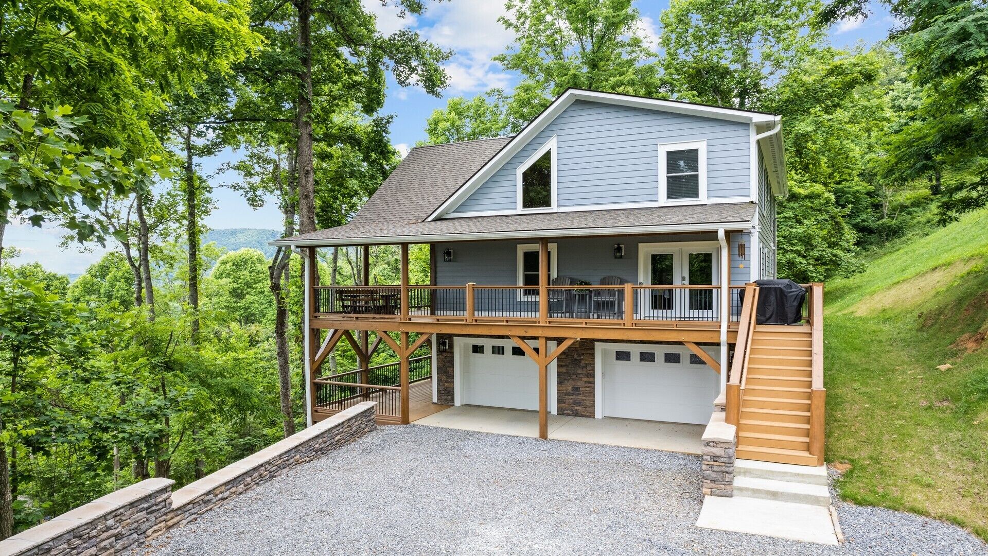 A two-story house with a covered porch, a stone foundation, and a gravel driveway.