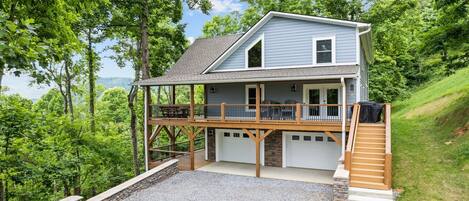 A two-story house with a covered porch, a stone foundation, and a gravel driveway.