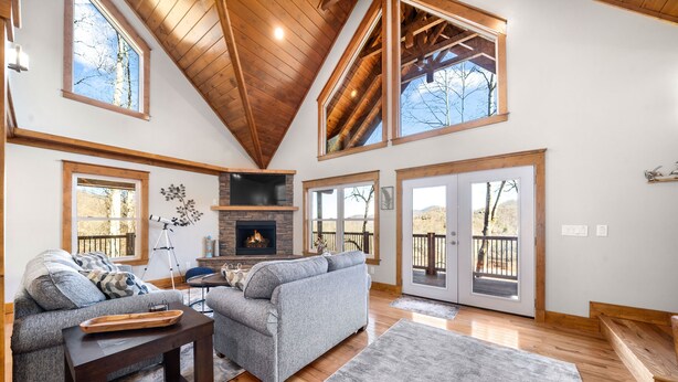 A spacious living room with a fireplace, large windows, and a high ceiling.
