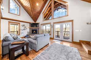 A spacious living room with a fireplace, large windows, and a high ceiling. - Braeburn/New Cabin/Views/Fireplace/Media Room (Waynesville)