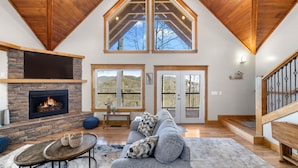 A spacious living room with a stone fireplace, a large gray sofa, and a wooden ceiling.