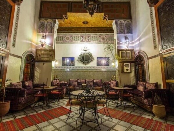 Cozy seating area with a round table and comfortable sofas and armchairs, surrounded by decorative tiles and artwork.