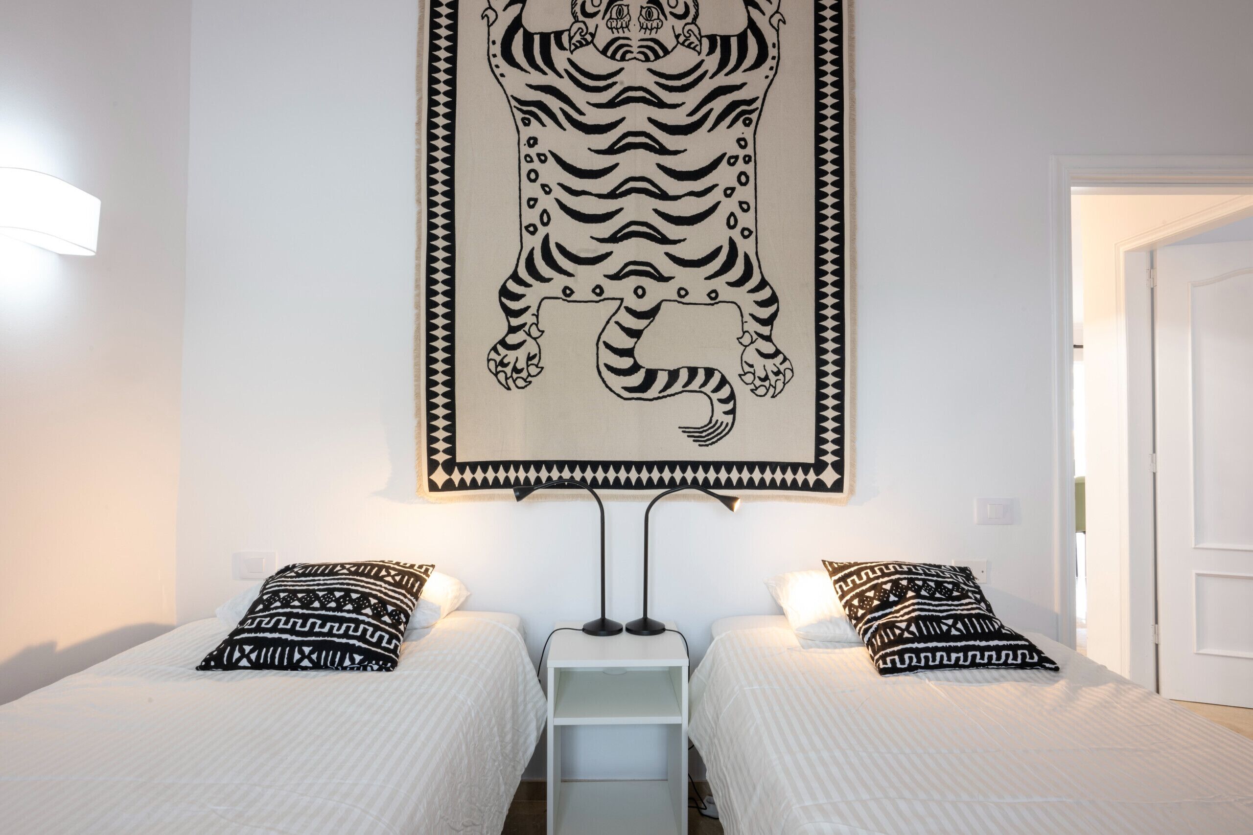 A room with two beds, each with patterned pillows, a wall-mounted tiger artwork, and a white door.