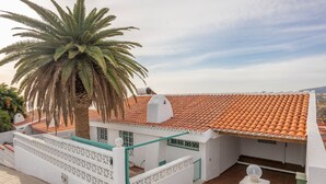 Un edifici blanc amb teulada de rajola, una palmera i una tanca blanca amb motius decoratius.