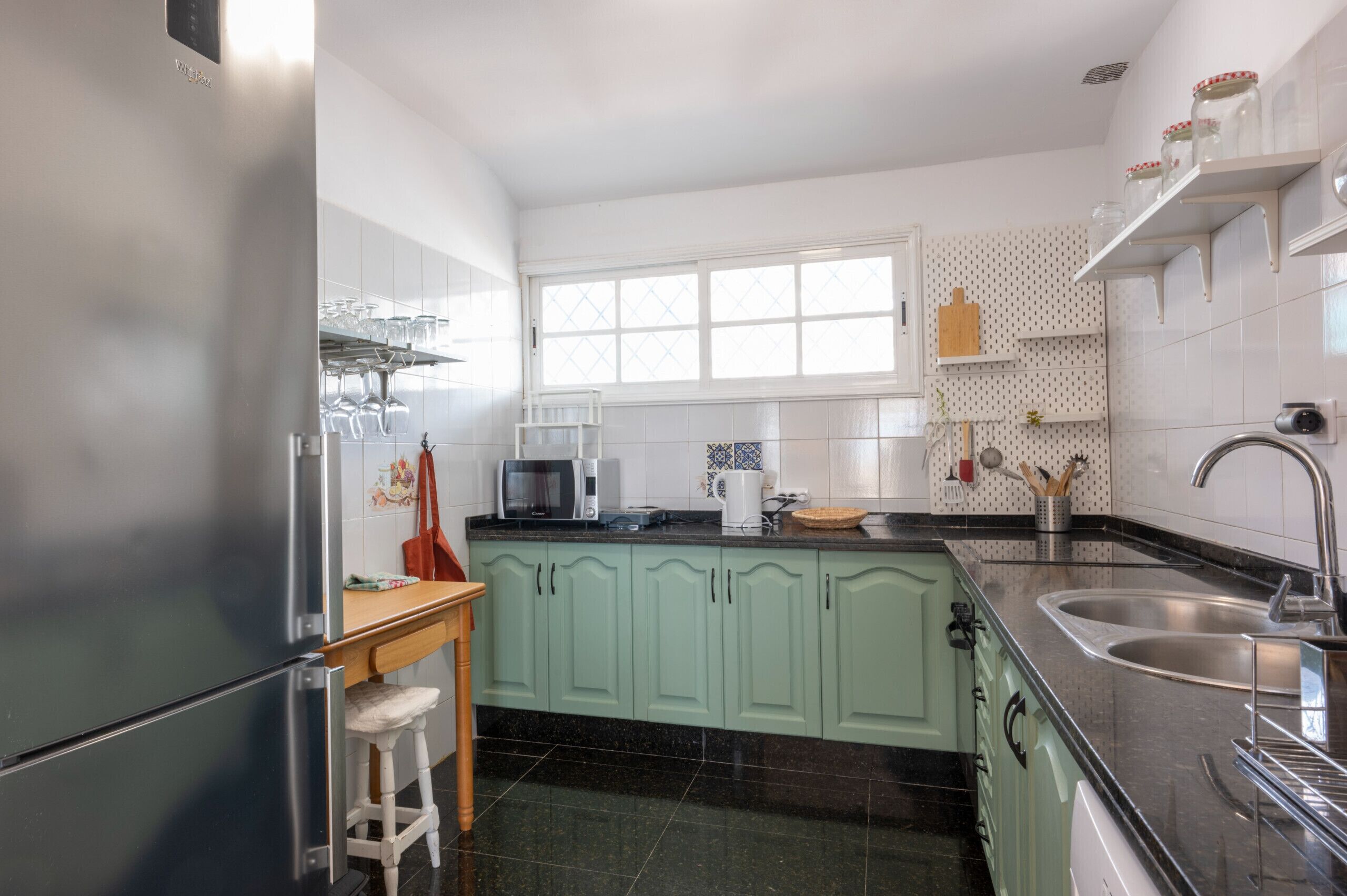 A kitchen with a refrigerator, microwave, sink, and green cabinets.