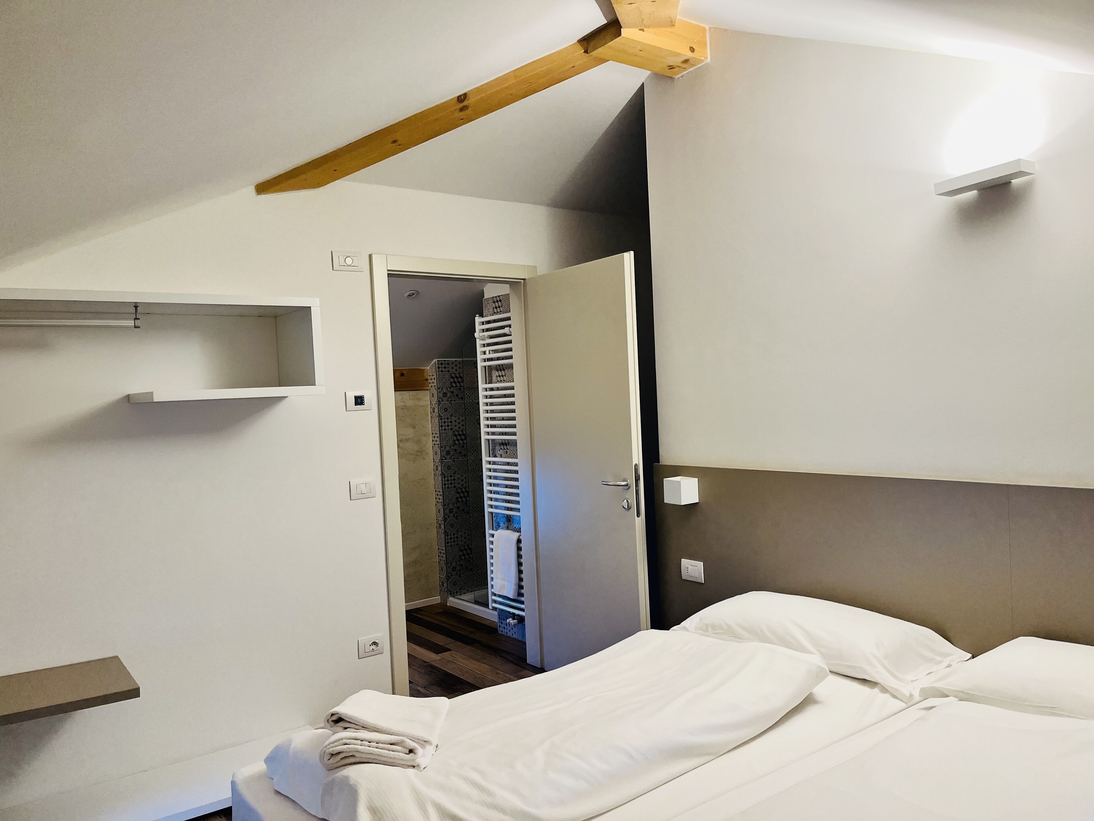 A bedroom with a bed, a wooden ceiling beam, a white wall, and a door leading to a bathroom.
