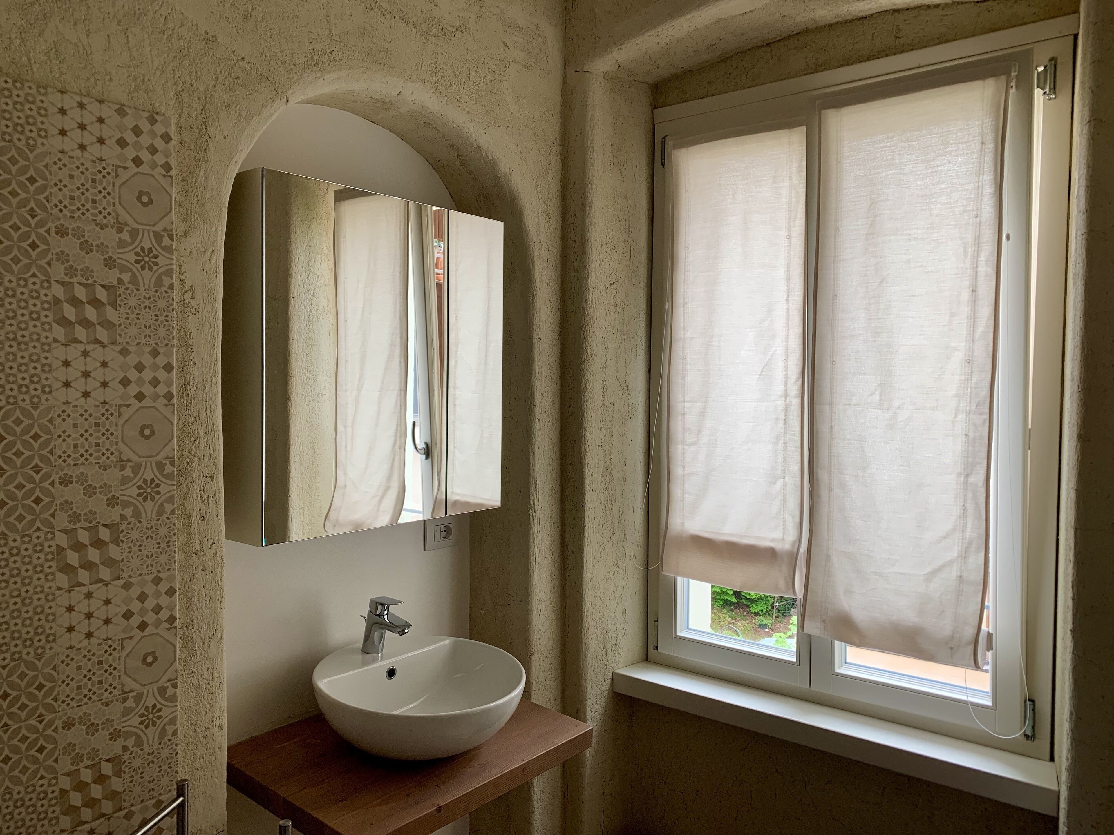 Casa de banho com uma pia branca, um espelho e uma janela com cortinas.