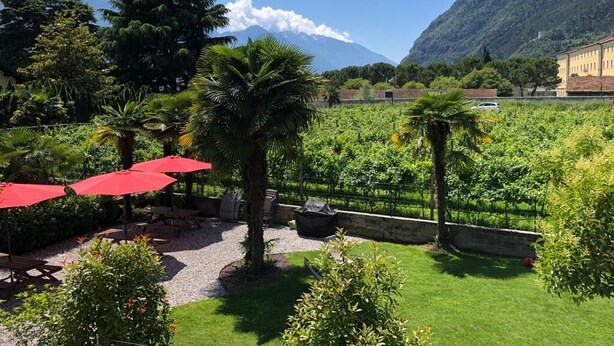 Un jardin luxuriant agrémenté de parasols rouges, un sentier de gravier et une chaîne de montagnes en arrière-plan.