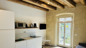 Une cuisine moderne avec des meubles blancs, un four à micro-ondes encastré, une bouilloire et une machine à café. La pièce comprend une petite table ronde et un canapé.