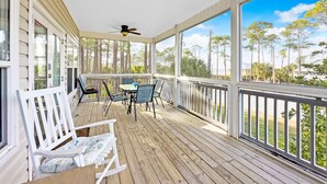 A covered porch with a table and chairs, large windows, and a ceiling fan.