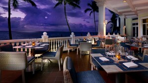 Un restaurante con terraza al aire libre y vistas al océano, con sillas y mesas de mimbre dispuestas con vajilla.