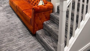 Una sala de estar moderna con un sofá naranja capitonado, una alfombra gris y una escalera con barandales blancos.