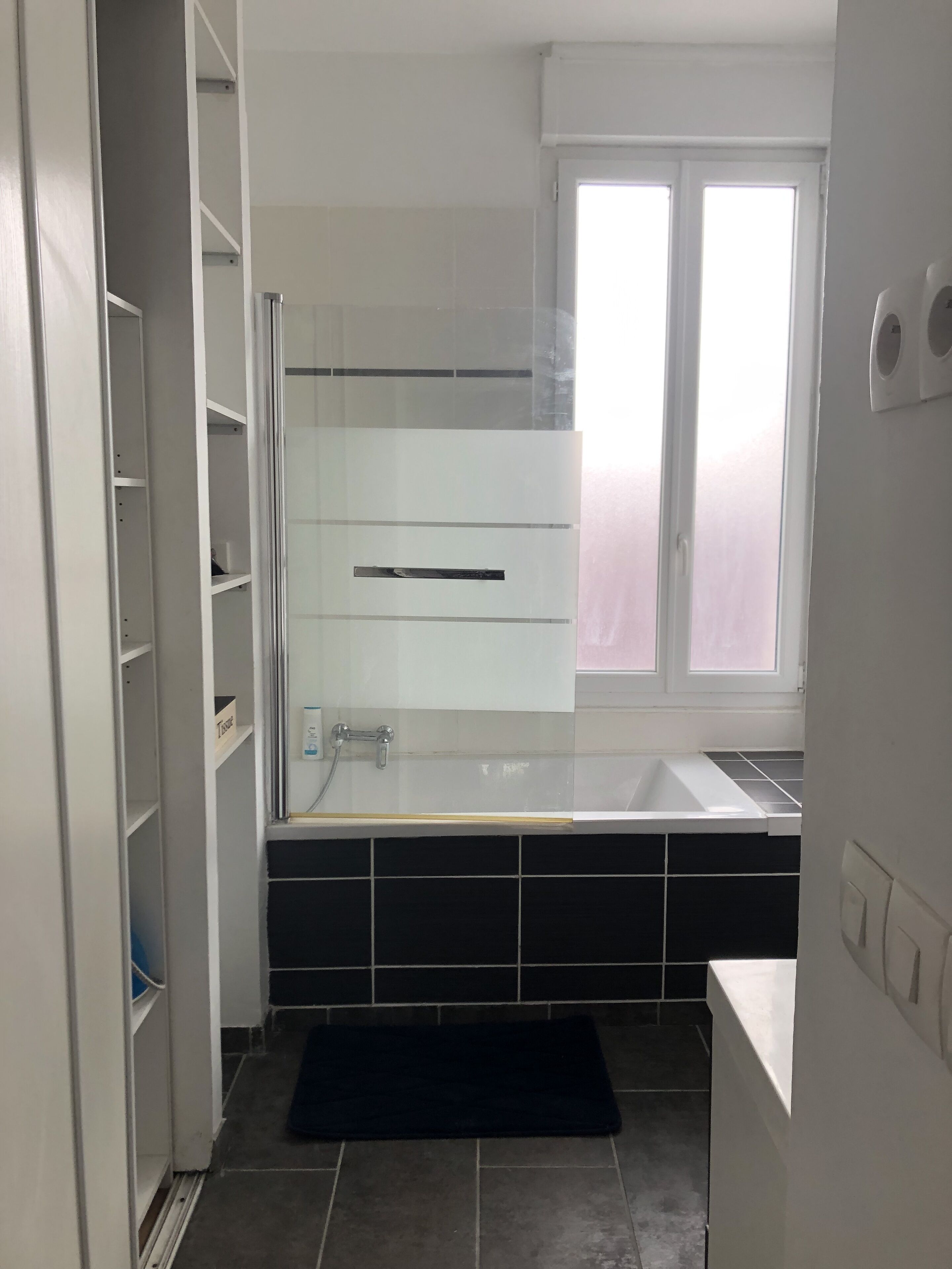 A modern bathroom with a glass shower enclosure, a white bathtub, and a window with frosted glass.