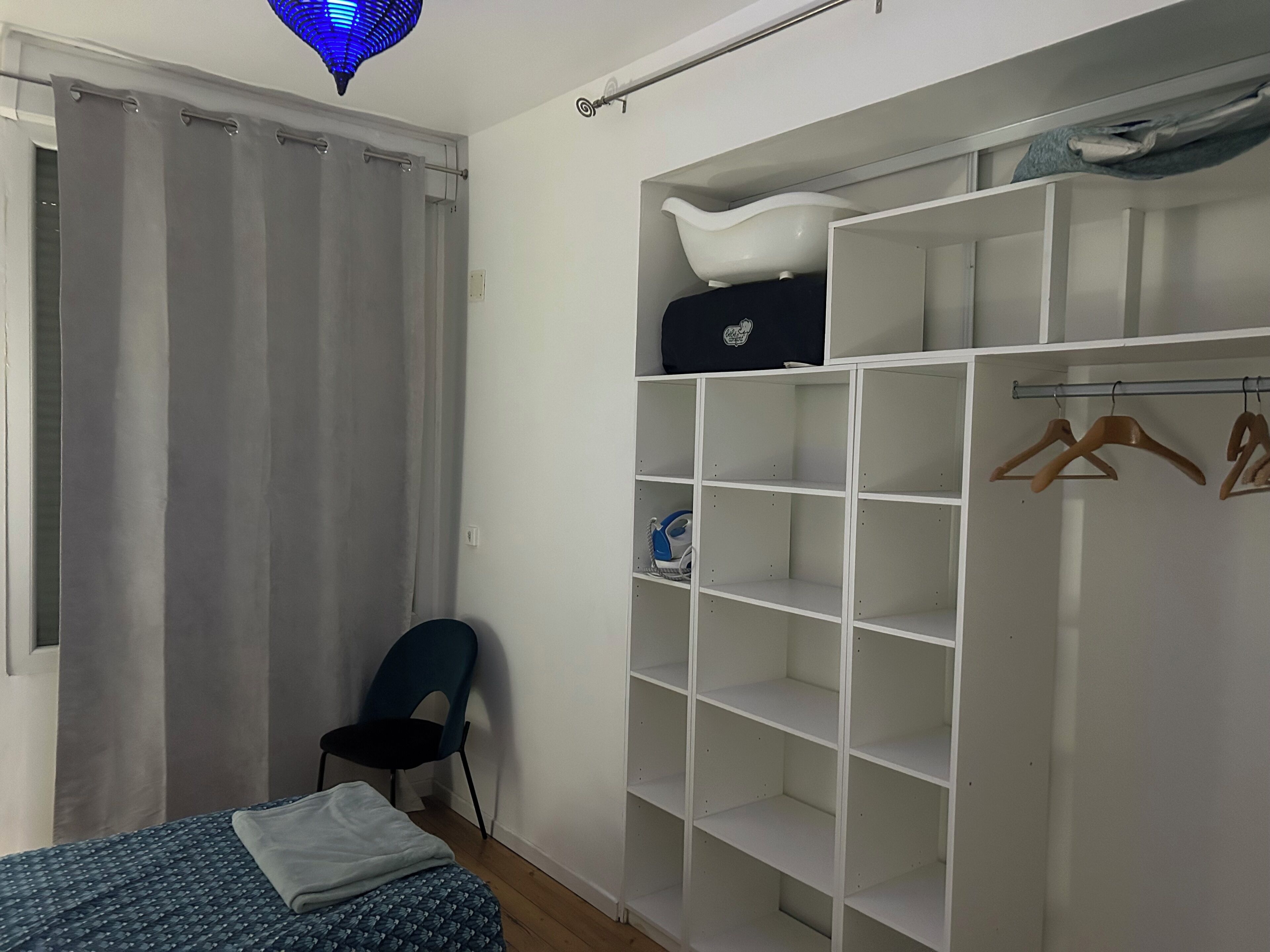Un dormitorio con cama, una silla, un armario y una lámpara colgante.