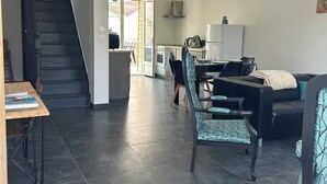 A modern living area with a staircase, dining table, chairs, a sofa, and a kitchen in the background. - Maison Tout Confort Avec Jacuzzi (Corbie)