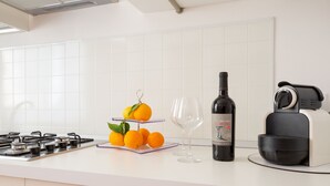 A kitchen counter with a gas stove, a wine bottle, a glass, and a fruit stand with oranges. - House in the historic center with private terrace and patio (Noto)