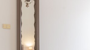 A bedroom with a large mirror, a bed with a white blanket, and a bedside table with a lamp. - House in the historic center with private terrace and patio (Noto)