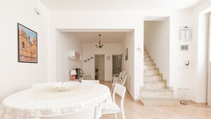 A dining area with a round table and chairs, a staircase, and a hallway leading to another room. - House in the historic center with private terrace and patio (Noto)